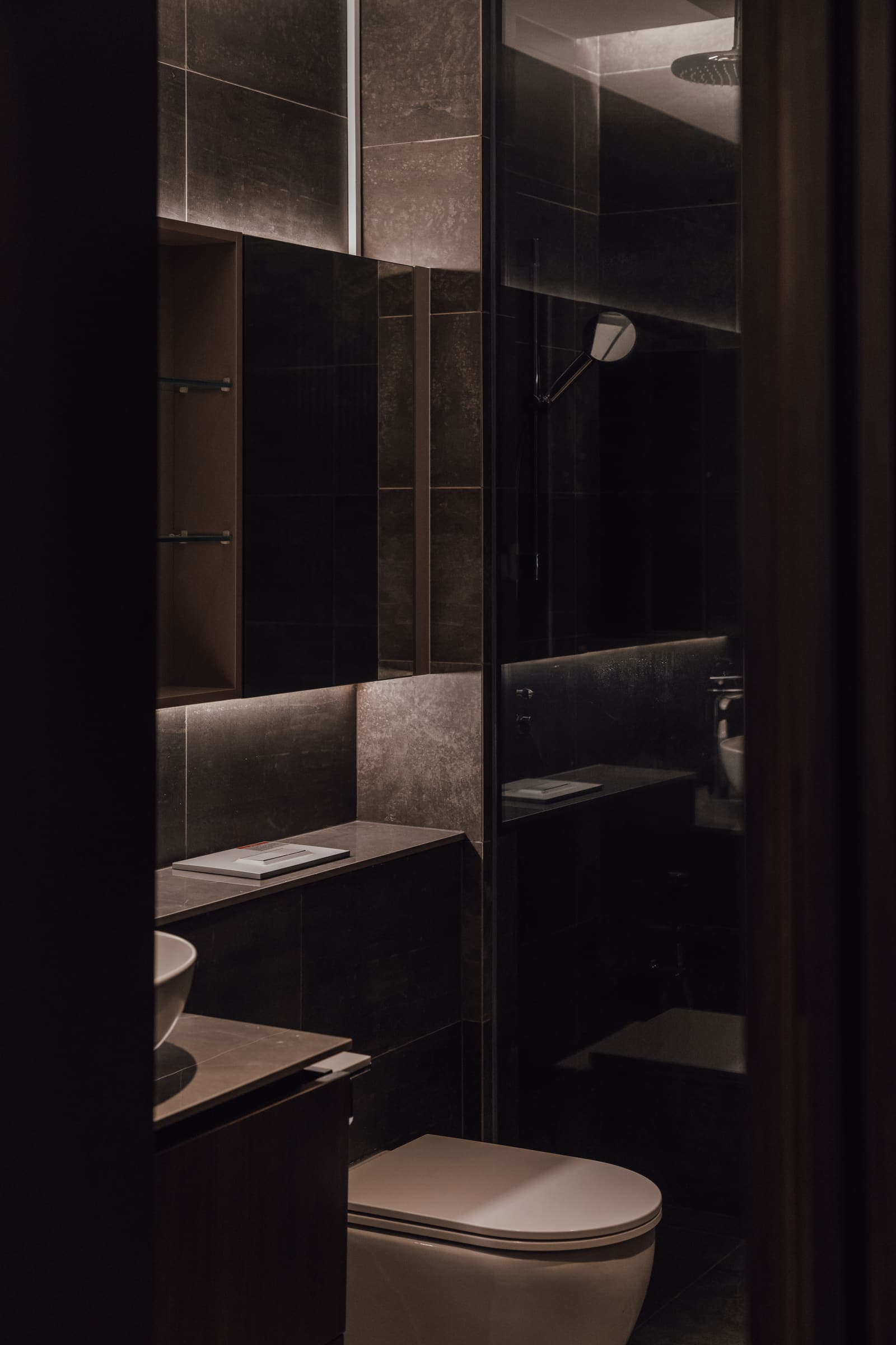 Bathroom seen through a doorway, with concealed lighting grazing the stone shelving and vanity.