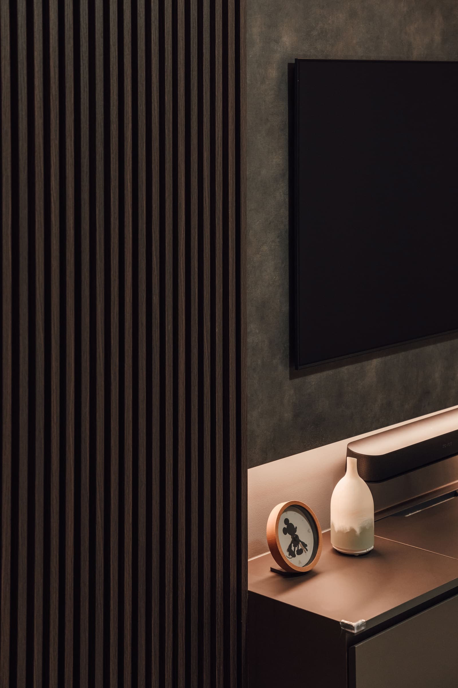 Console detail beside a fluted timber wall, a warm lamp picking out a framed photograph and vase.