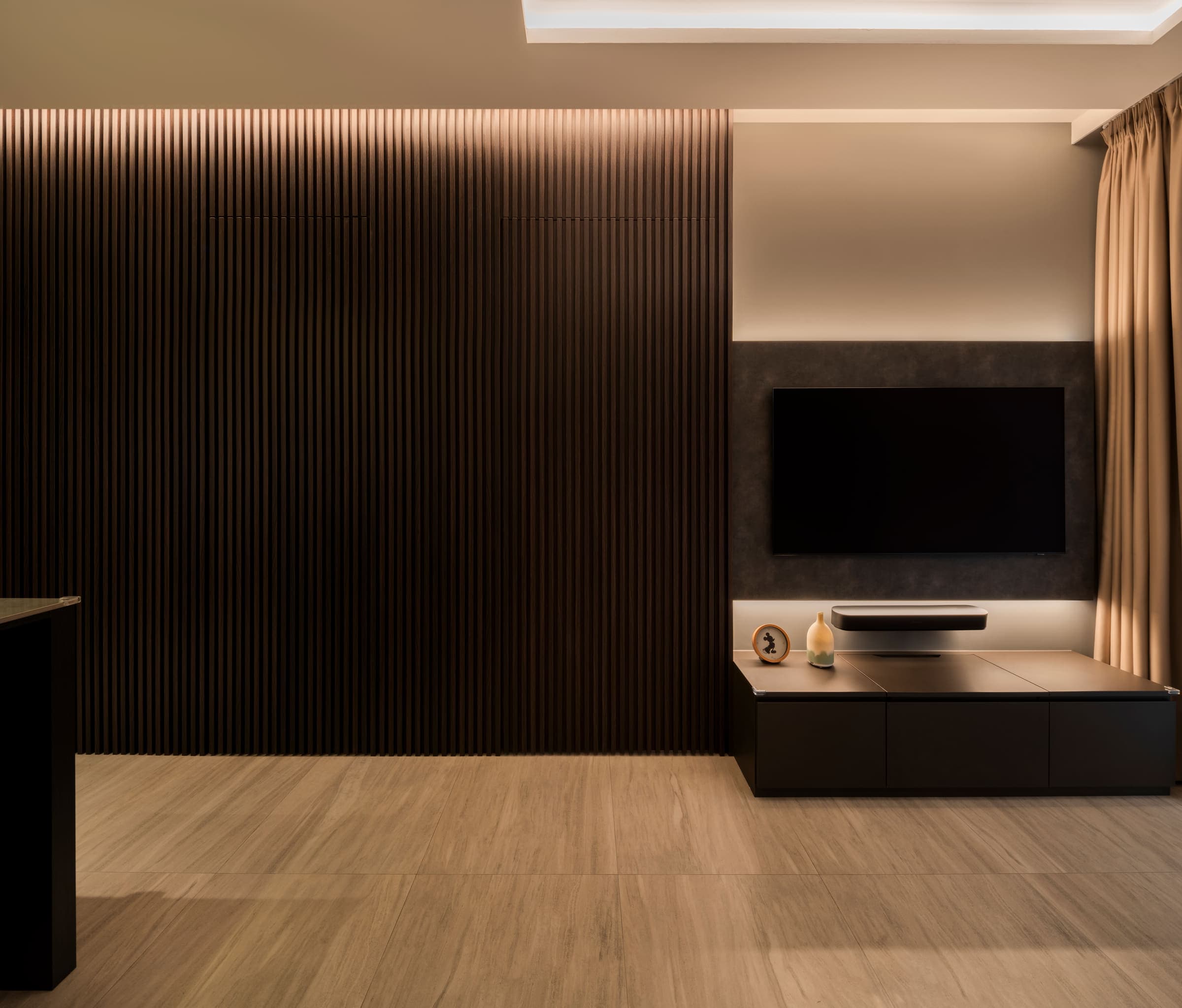 The living room's fluted wall and media console under warm white light, the first of three settings of the same scene.