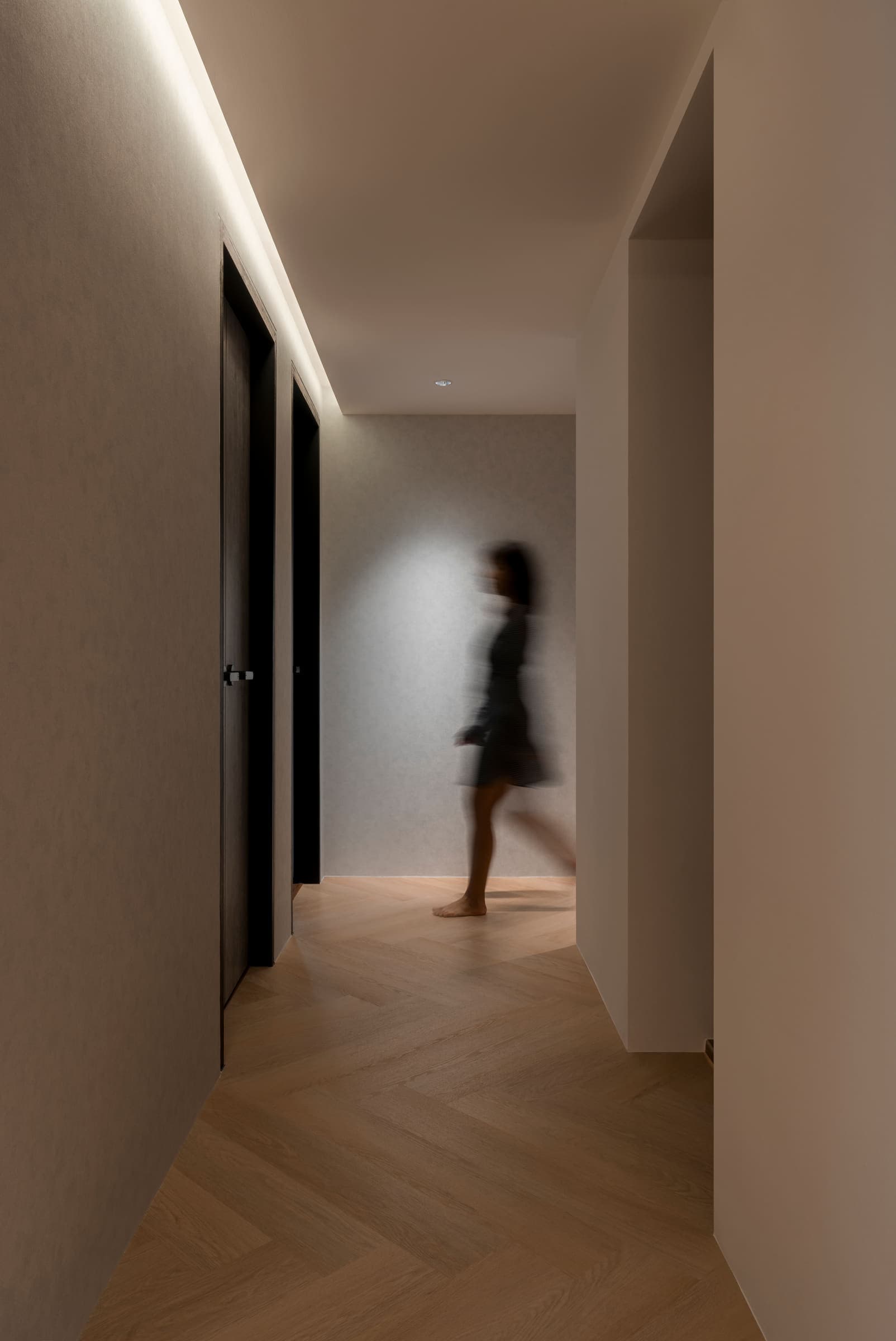 Corridor lit only by a concealed cove along one wall, a figure walking through it.